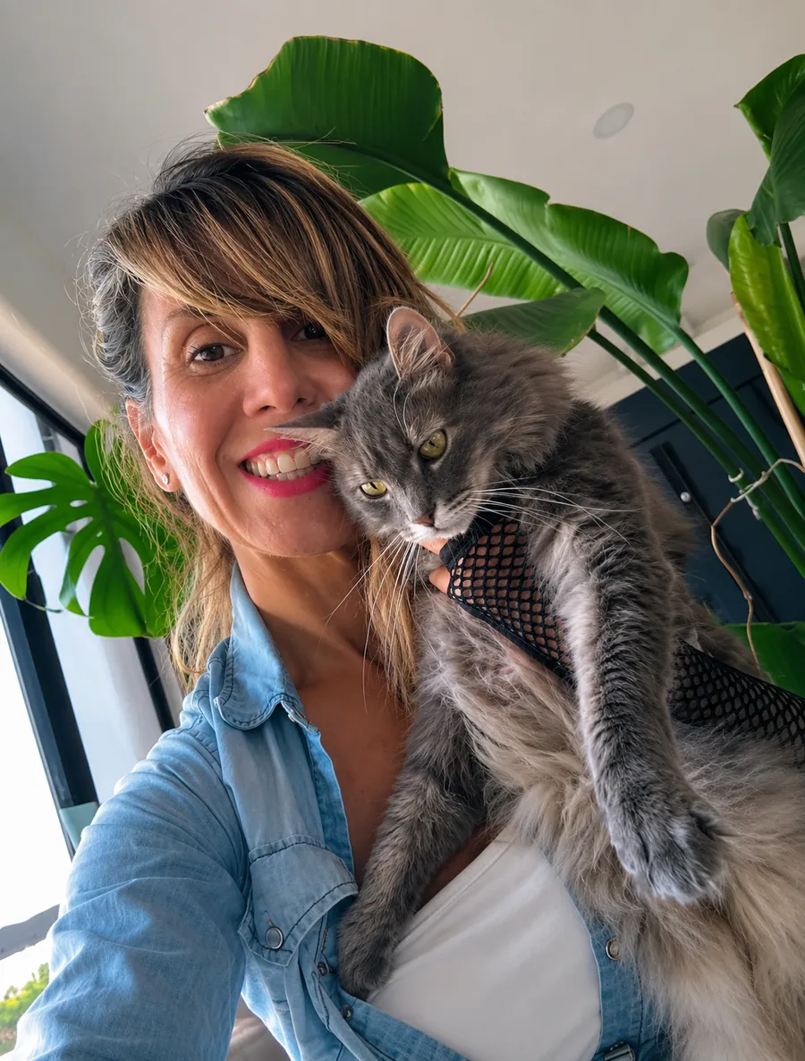 Faby, pet sitter, sonriendo con un gato gris de pelo largo en brazos
